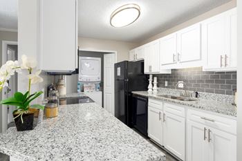 A kitchen with granite counters, white cabinets and a laundry closet with stackable washer and dryer.